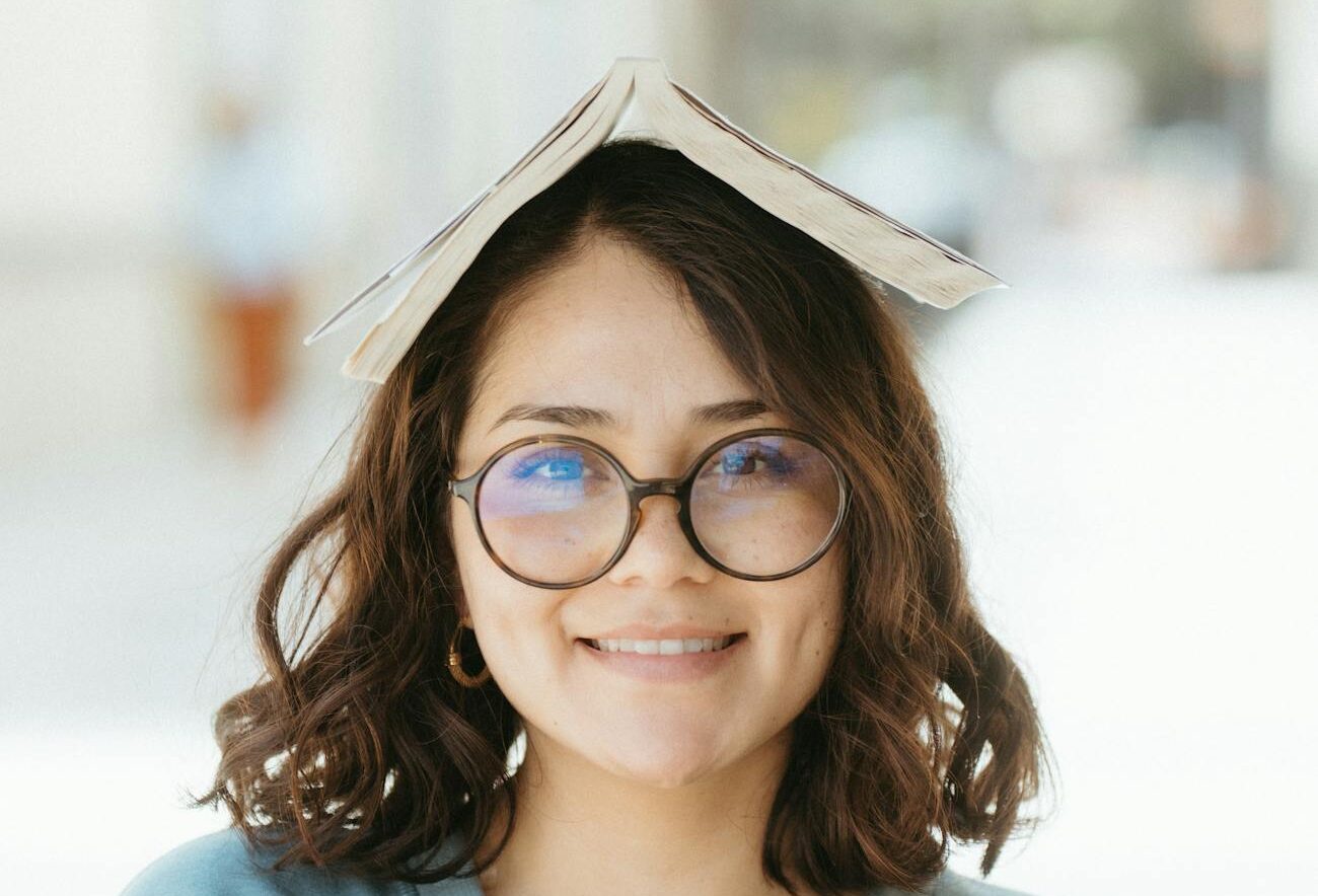 smiling woman with book on head outdoors