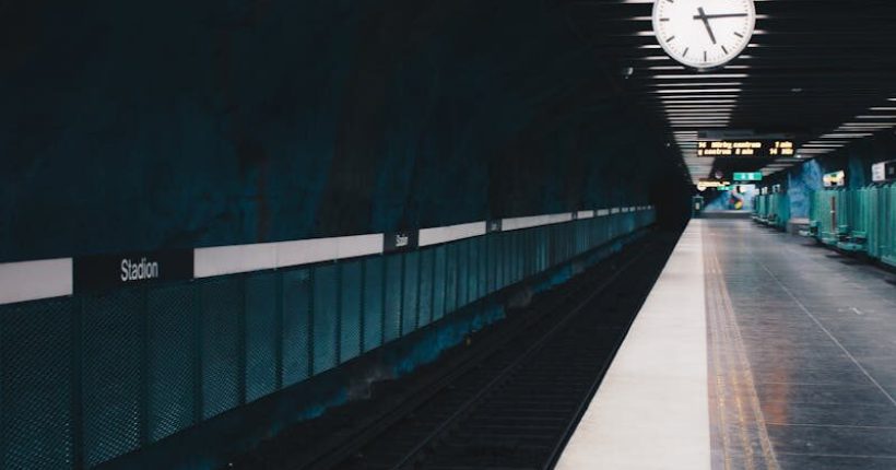 A moody view of an empty subway station in Stockholm with a large clock on the ceiling.