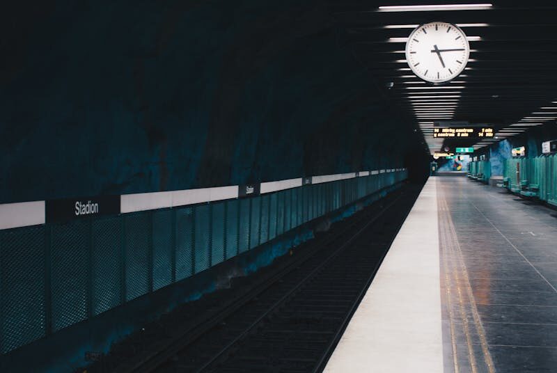 A moody view of an empty subway station in Stockholm with a large clock on the ceiling.