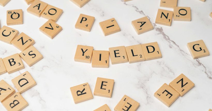 Scrabble tiles forming the word 'YIELD' on a marble surface, symbolizing finance and investment.
