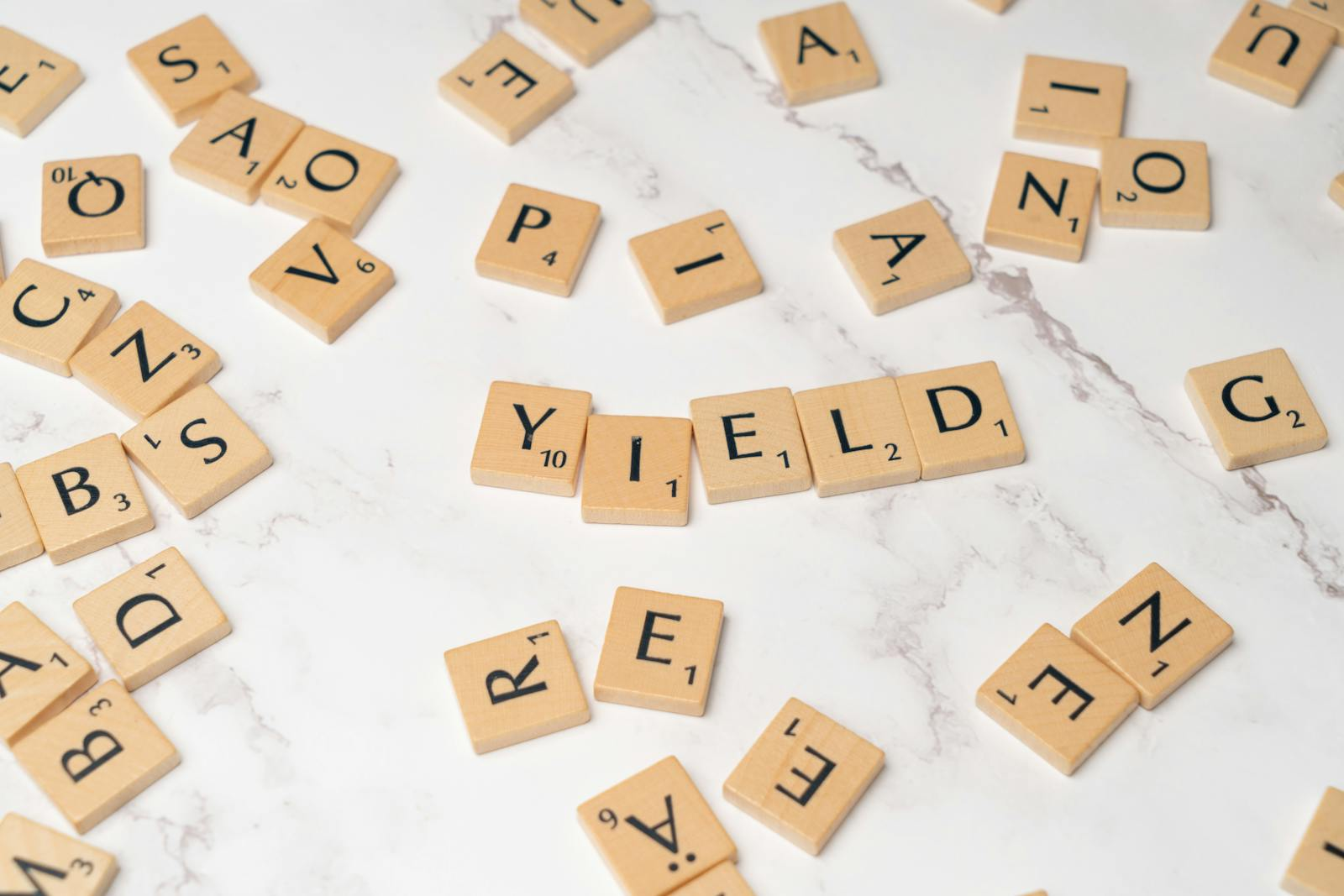 Scrabble tiles forming the word 'YIELD' on a marble surface, symbolizing finance and investment.