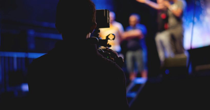 A cameraman films a live concert performance, capturing the dynamic stage action.