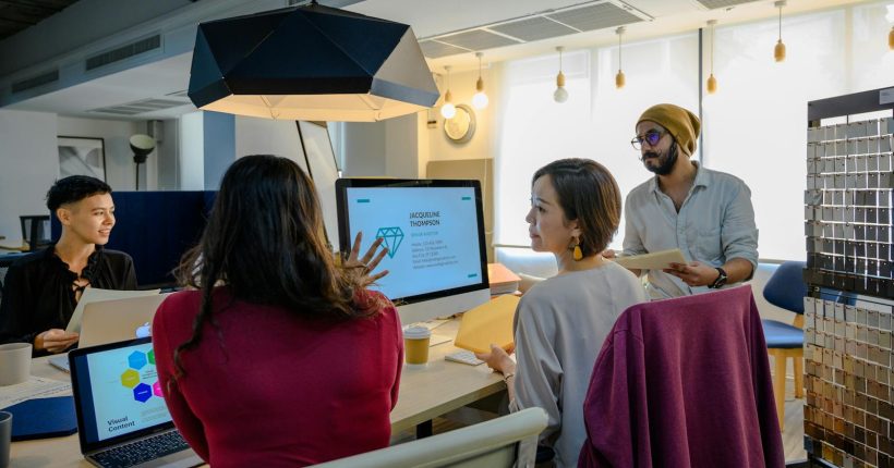 A diverse group of professionals working together in a contemporary office setting using laptops and a monitor.