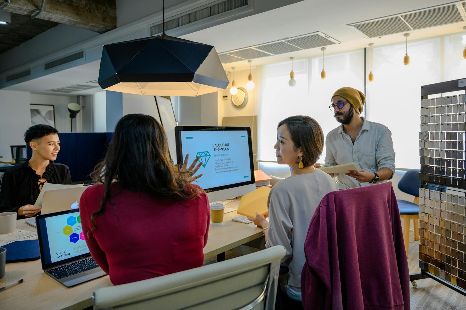 A diverse group of professionals working together in a contemporary office setting using laptops and a monitor.