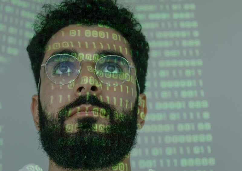A bearded man with eyeglasses analyzing data in a digital environment with green binary code projections.