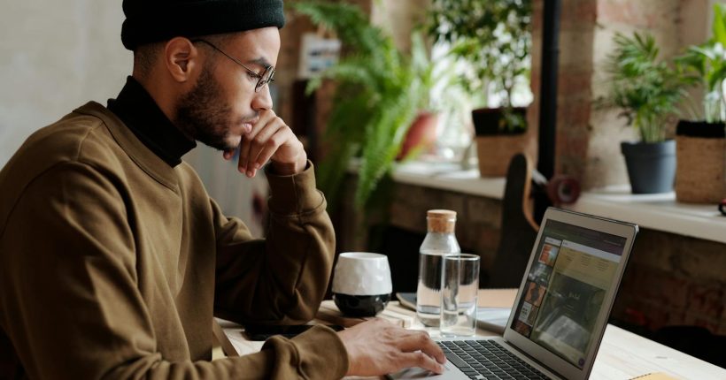A stylish young man works remotely on his laptop in a cozy indoor workspace.