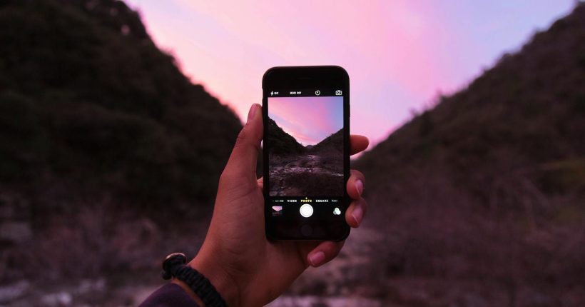 A person photographs a stunning sunset landscape with a smartphone in nature.