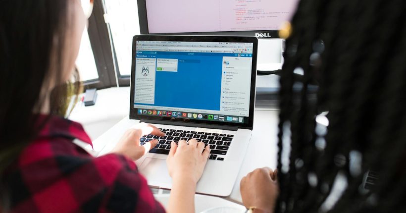 Two women working together on a laptop in a bright, modern office setting.