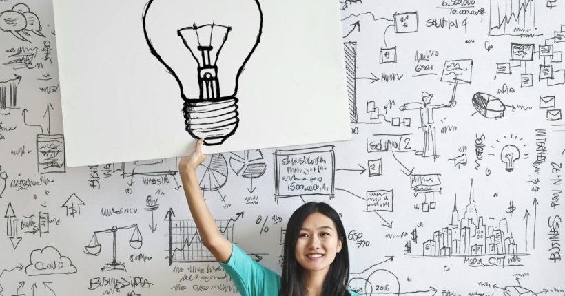 Young woman holds a light bulb drawing against a creative brainstorming wall.