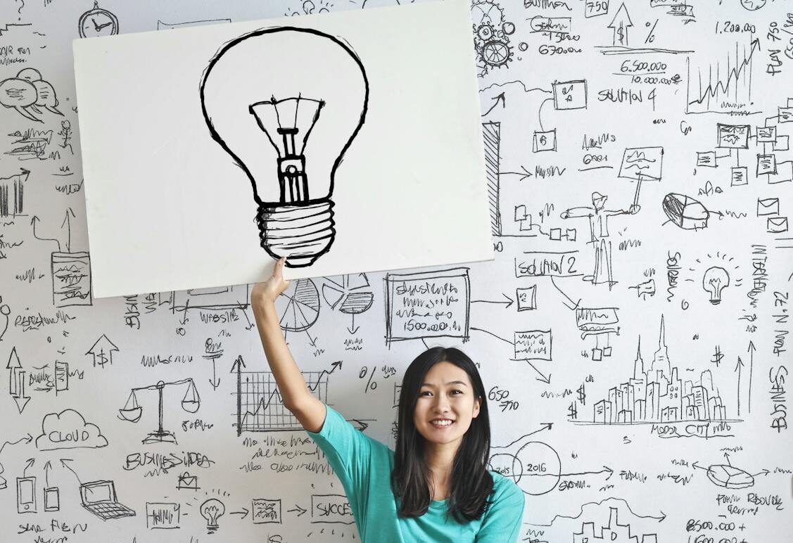 Young woman holds a light bulb drawing against a creative brainstorming wall.