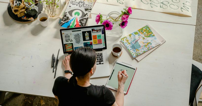 Artistic workspace featuring calligraphy and digital design on a tablet and laptop.