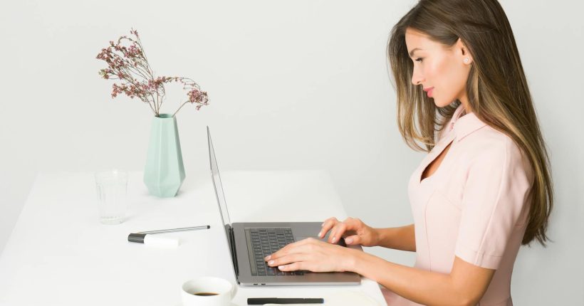 A woman in a pink dress working on a laptop at a modern, minimalist desk.