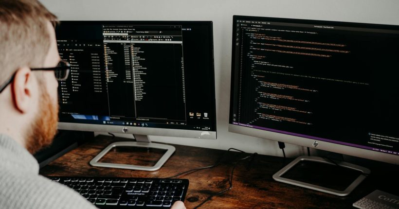 Software developer working on code with dual monitors in a home office setting.