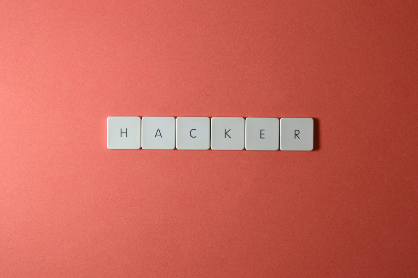 Close-up of the word 'HACKER' made with letter tiles on a red background, emphasizing cybersecurity.