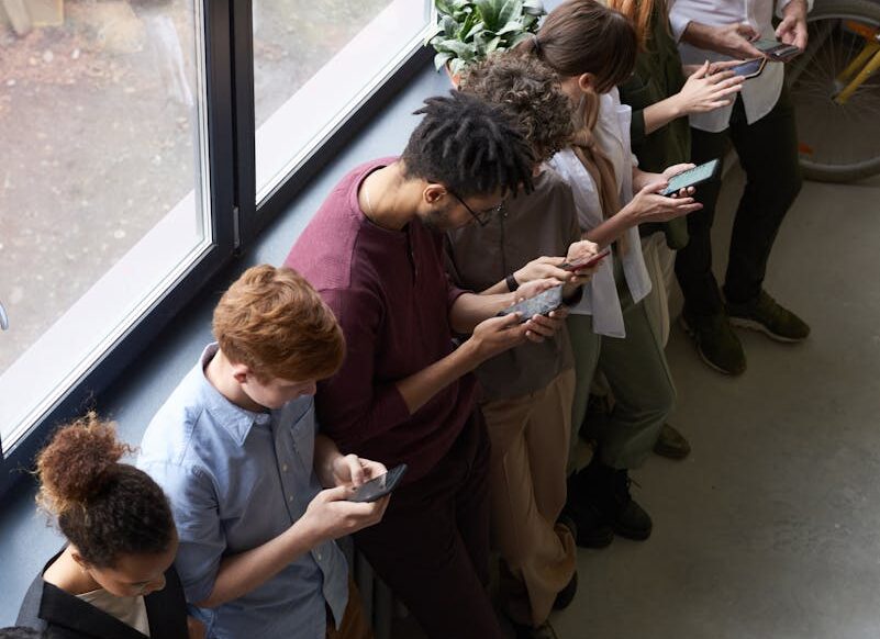 A group of diverse office workers standing by a window using smartphones, capturing modern workplace connectivity.