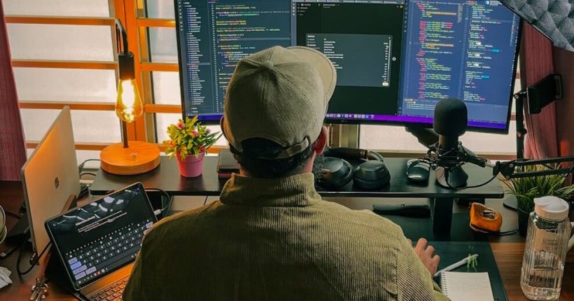 A developer's home office setup with multiple screens, coding in progress, and cozy lighting.