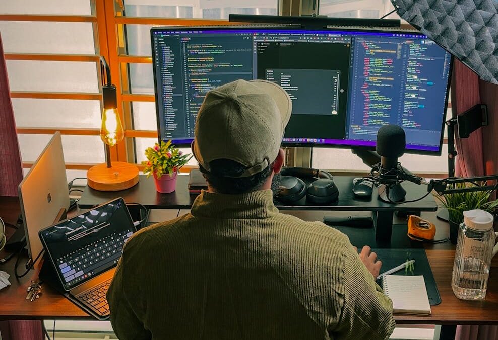 A developer's home office setup with multiple screens, coding in progress, and cozy lighting.