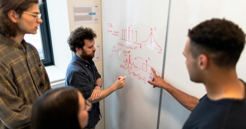 Group of engineers discussing data on a whiteboard during a team meeting.
