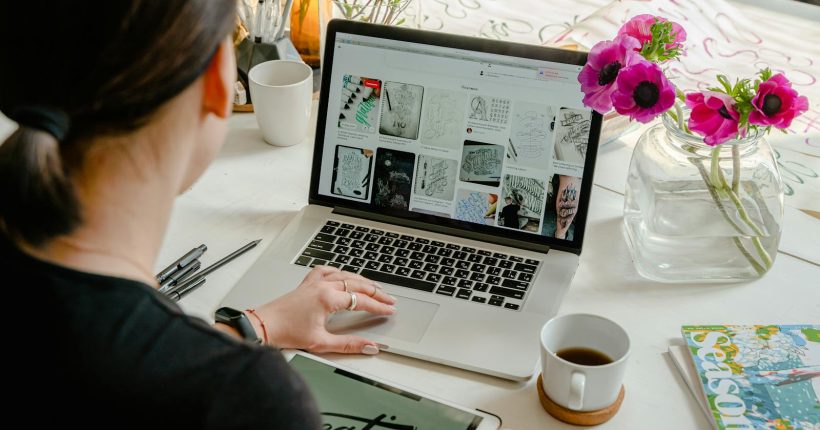 Woman in a creative workspace using a laptop and tablet for calligraphy. Artistic and tech-driven environment.