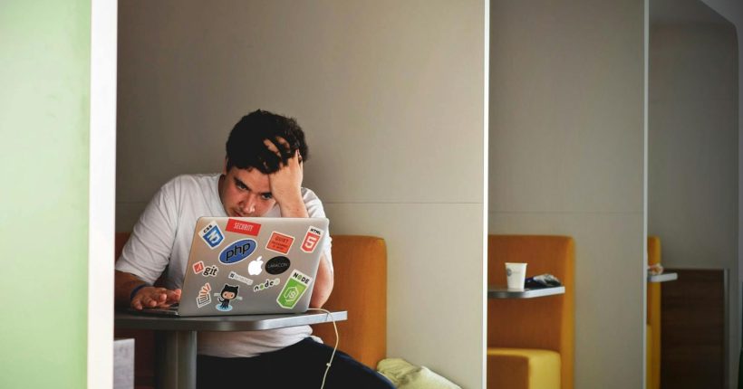 Man showing stress and frustration while working remotely on a laptop indoors.