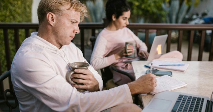 A couple working together on their laptops while enjoying a coffee outdoors.