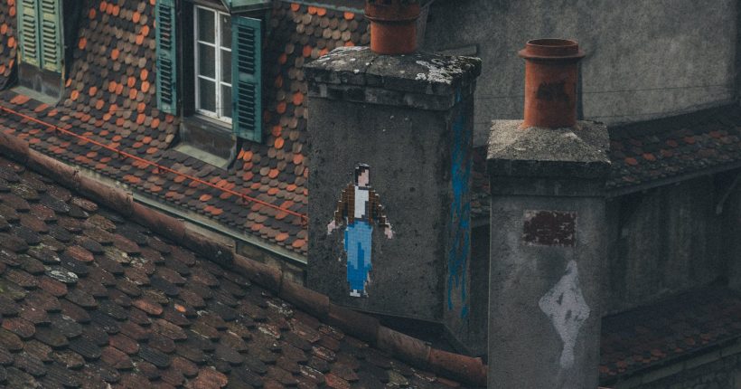 A rustic rooftop featuring unique pixel art graffiti on a chimney in an urban setting.