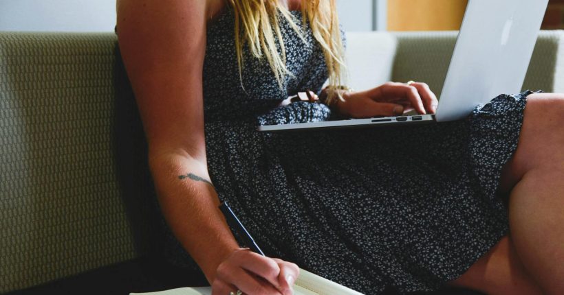 A woman multitasking with a laptop and writing notes, highlighting remote work and study.
