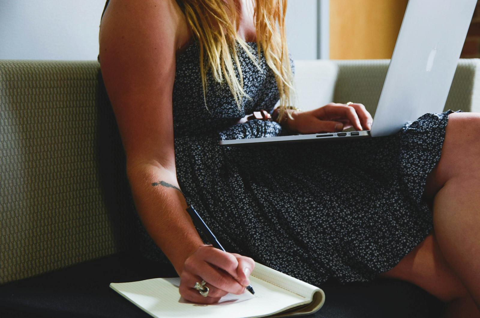 A woman multitasking with a laptop and writing notes, highlighting remote work and study.