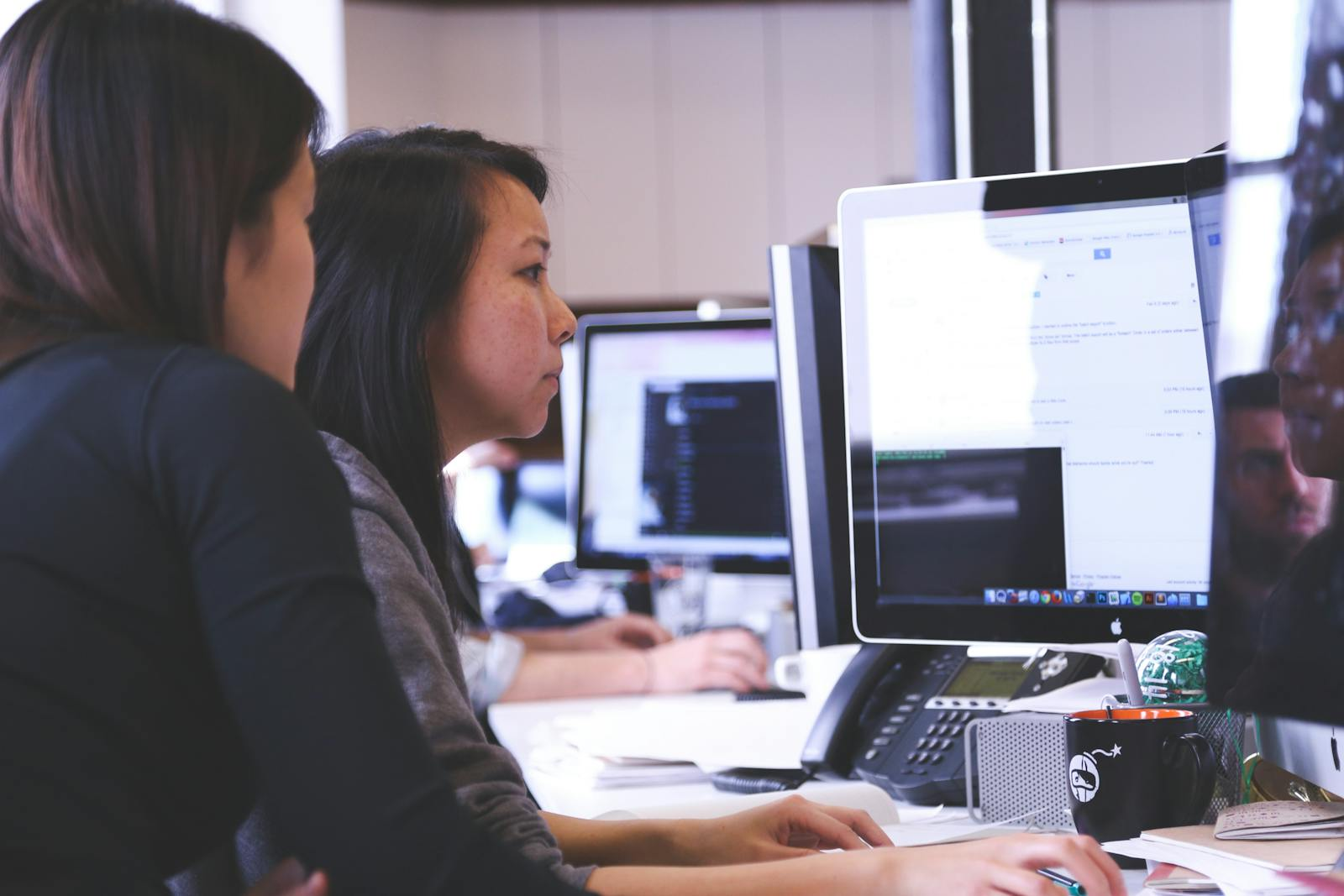Two women working together on code at a computer in a modern office setting.