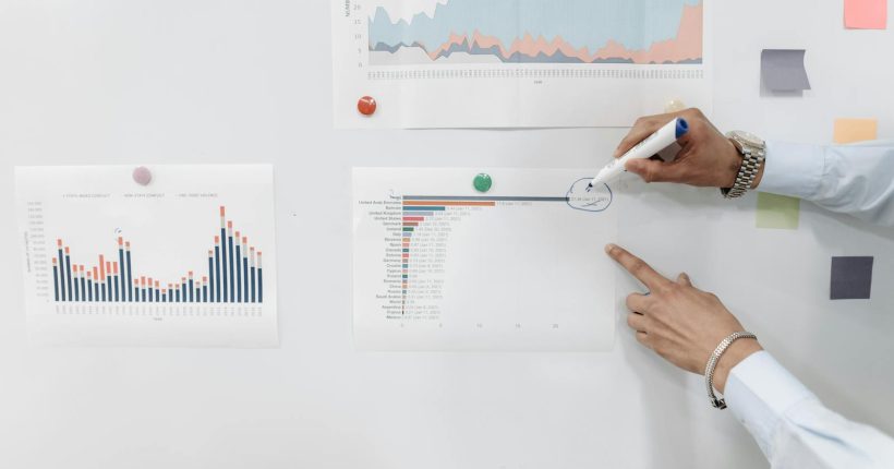 Hands pointing at charts and graphs on a whiteboard during a business meeting presentation.