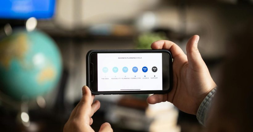 Close-up of hands holding a smartphone displaying a business planning cycle diagram.
