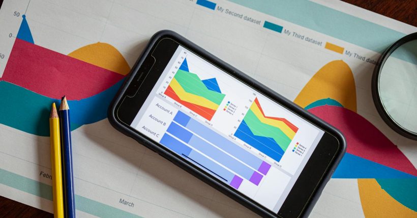 Overhead view of a smartphone displaying colorful charts on paper graphs, symbolizing mobile data analysis.