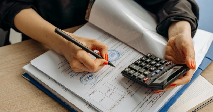 An accountant using a calculator and signing paperwork, showcasing financial analysis.