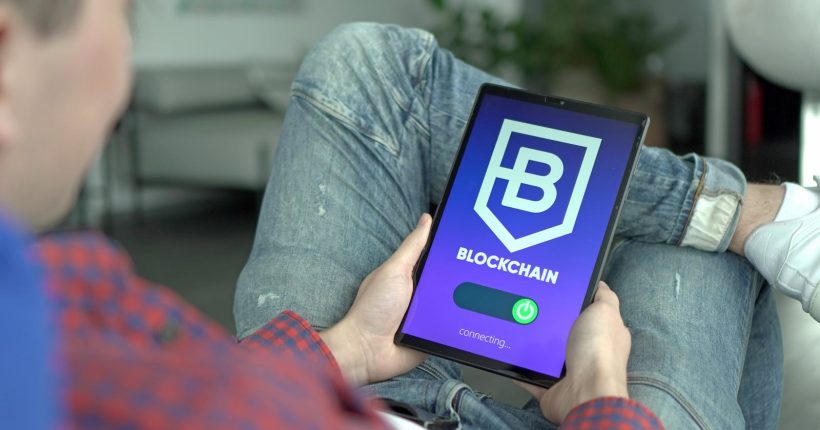 Adult holding a digital tablet displaying a blockchain application interface.