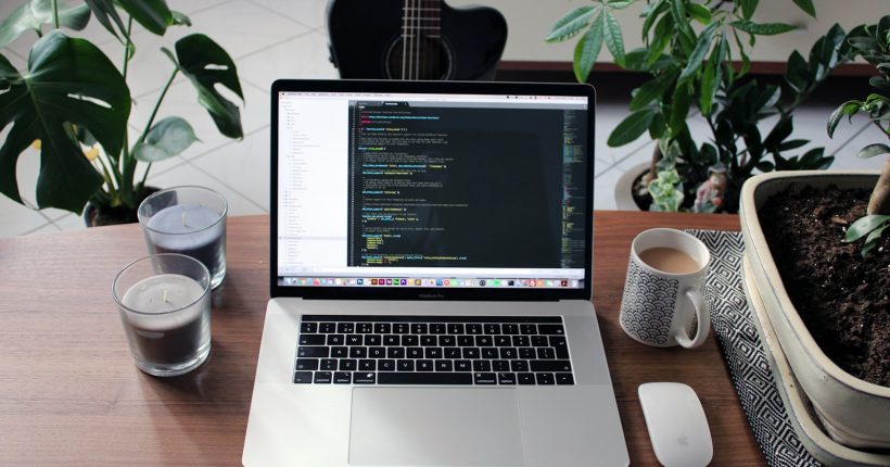 macbook pro beside white ceramic mug on brown wooden table