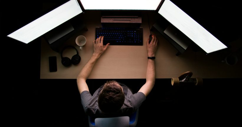 man facing three computer monitors while sitting