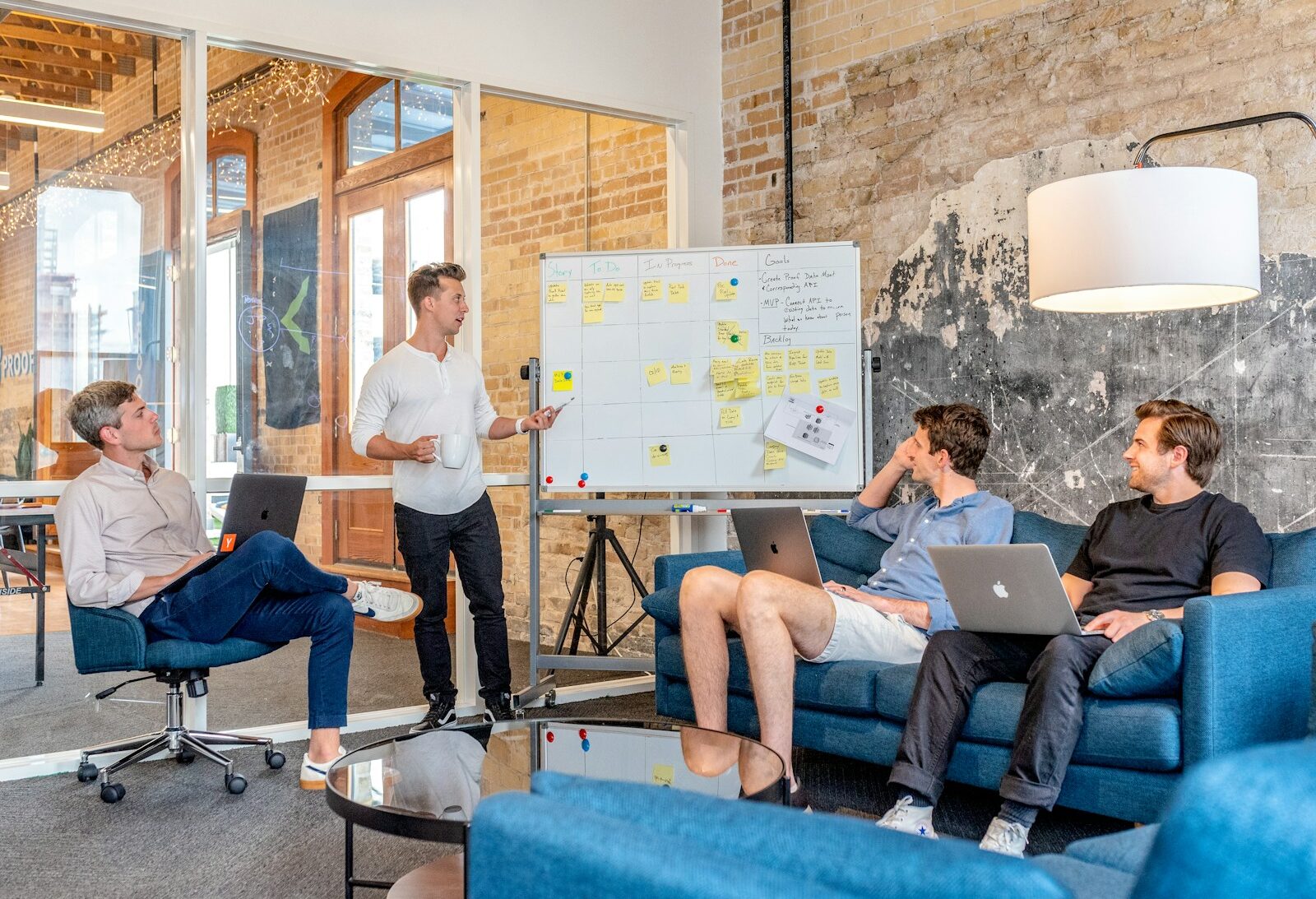 three men sitting while using laptops and watching man beside whiteboard