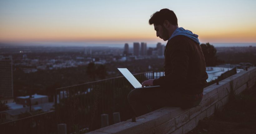 man sitting on concrete brick with opened laptop on his lap