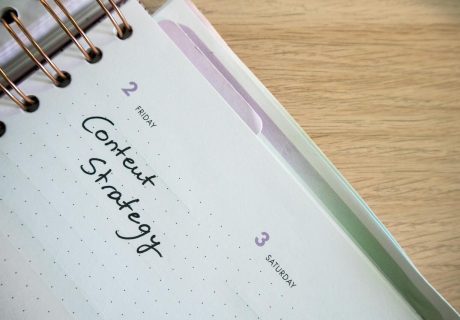 Top view of a notebook open to a day planner featuring 'Content Strategy' handwritten, lying on a wooden desk.