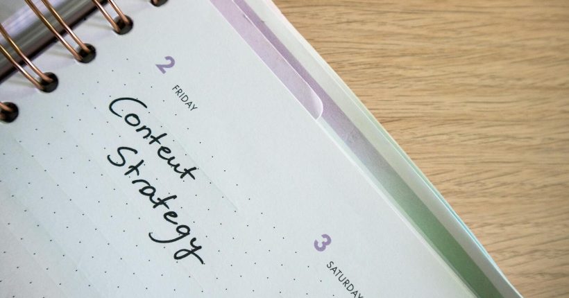 Top view of a notebook open to a day planner featuring 'Content Strategy' handwritten, lying on a wooden desk.