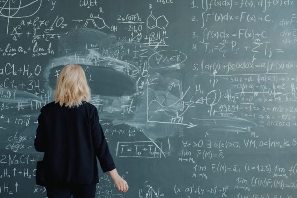 Woman looking at a blackboard with complex math equations.