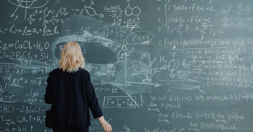 Woman looking at a blackboard with complex math equations.