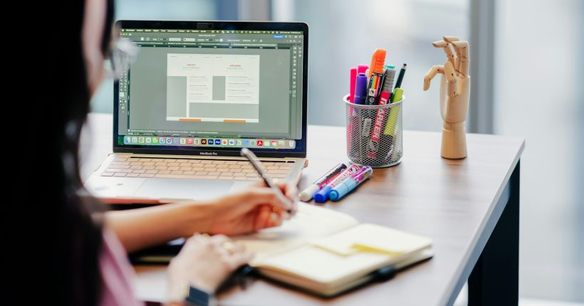 Woman working on laptop and notebook at desk.