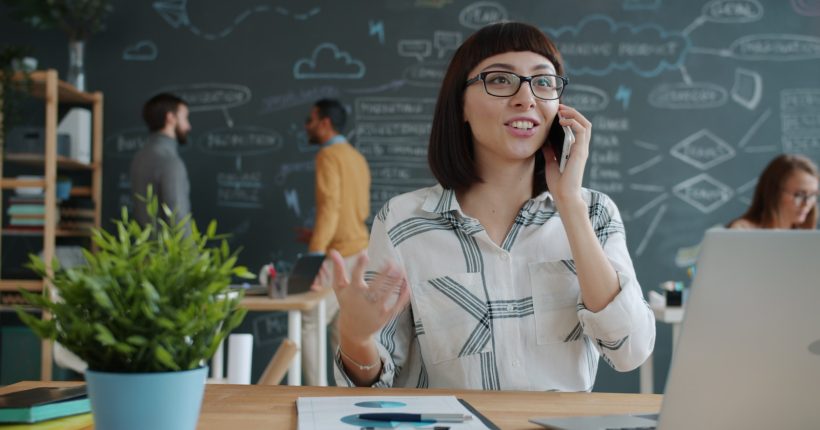 Woman talking on phone in modern office with chalkboard wall.