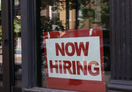 A "now hiring" sign hangs in a store window.