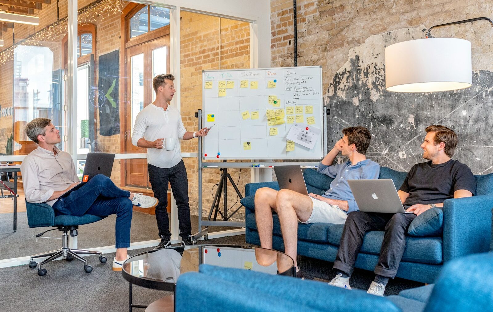 three men sitting while using laptops and watching man beside whiteboard