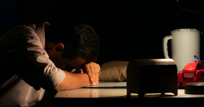 Man resting head on desk in dark room