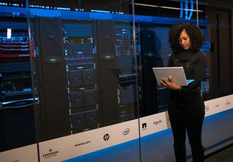 A female engineer using a laptop while monitoring data servers in a modern server room.