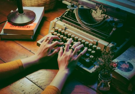 A cozy scene with a vintage typewriter and hands typing indoors beside books and flowers.