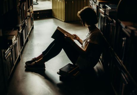 A young woman engrossed in a book, sitting on the floor of a quiet library, creating a cozy reading atmosphere.